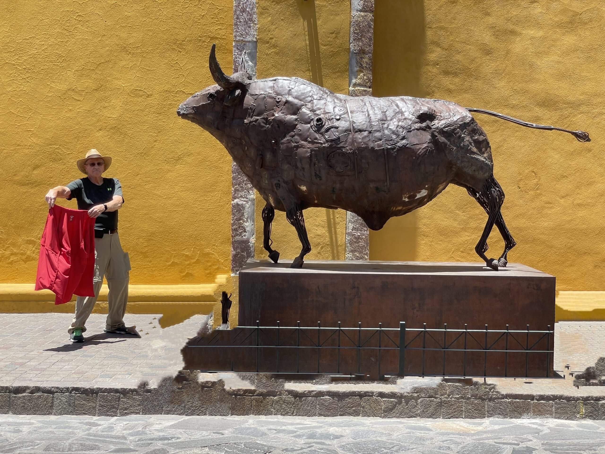 EJK holding a red shirt in front of a statue of a bull symbolizing a bull fight